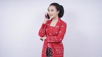 beleza asiática em kebaya no telefone via smartphone isolado no fundo branco foto