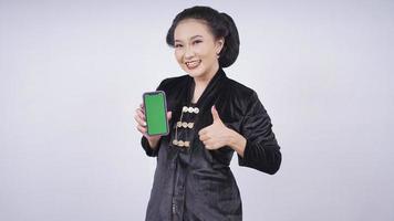 beleza asiática em kebaya mostrando o gesto ok da tela do smartphone isolado no fundo branco foto