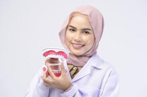 dentista feminino muçulmano segurando aparelho invisalign sobre estúdio de fundo branco, saúde bucal e conceito ortodôntico. foto