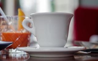 bebida de café quente em um copo branco sobre uma mesa de madeira em um fundo desfocado de um interior de café. bebida de café com cafeteria turva como pano de fundo. foto selecione o foco.