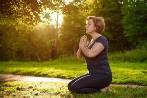 mulher adulta medita com as palmas das mãos dobradas no parque com os olhos fechados foto