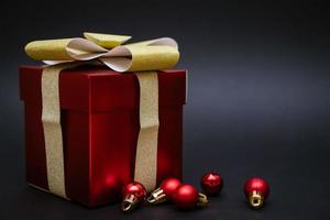 caixa de presente vermelha com bolas para decorar uma árvore de natal em um fundo preto foto