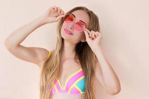 close-up de menina feliz em óculos de sol rosa isolados. férias de verão e fim de semana divertido. conceito de verão. jovem sorridente em maiô de moda. foco seletivo. roupa de verão de praia. espaço de cópia foto