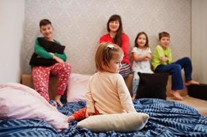 grande família feliz está se divertindo juntos no quarto. grande conceito de manhã familiar. mãe com quatro filhos usa pijama na cama em casa. foto