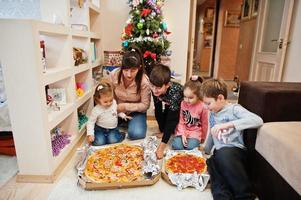 família feliz com quatro filhos comendo pizza em casa. foto