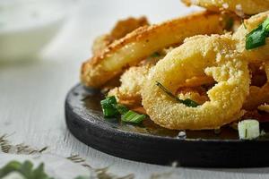 anéis de cebola em massa polvilhada com verduras em um fundo branco em um borrão. comida insalubre, mas deliciosa. foto