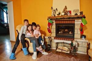 felizes quatro filhos em casa por uma lareira na sala de estar quente em dia de inverno. foto