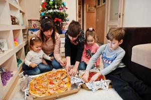 família feliz com quatro filhos comendo pizza em casa. foto