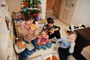 família feliz com quatro filhos comendo pizza em casa. foto