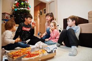 família feliz com quatro filhos comendo pizza em casa. foto