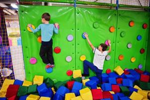 dois irmãos crianças subindo em uma parede verde no playground de atração. foto