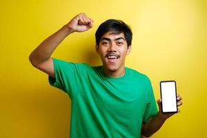 retrato de feliz jovem asiático em camiseta verde, apontando para o celular foto