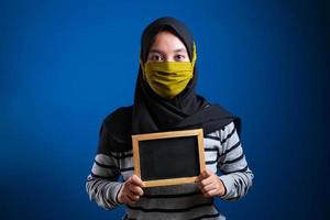 retrato de jovem asiática usando máscara protetora contra o coronavírus, segurando um pequeno quadro-negro foto