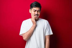 jovem bonito vestindo camiseta branca em cima tocando a boca com a mão com expressão dolorosa por causa de dor de dente ou doença dental nos dentes. dentista foto