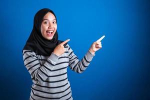 aluna asiática muçulmana sorrindo e apontando para apresentar algo do lado dela foto