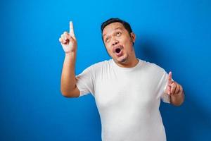 retrato de um homem asiático gordo engraçado em t-shirt branca sorrindo e dançando alegremente, alegre expressando comemorando boas notícias vitória ganhando gesto de sucesso contra fundo azul foto