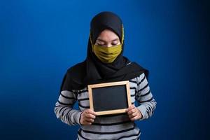 retrato de jovem asiática usando máscara protetora contra o coronavírus, segurando um pequeno quadro-negro foto