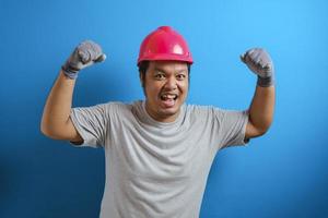 retrato de homem asiático gordo engraçado usando capacete vermelho sorrindo orgulhosamente ao mostrar pose de bíceps duplo, força sobre o conceito de confiança foto