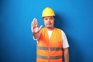 trabalhador asiático gordo vestindo colete de segurança laranja e capacete amarelo fazendo gesto de parada foto