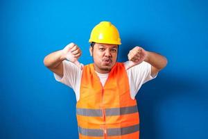 jovem operário asiático gordo vestindo colete de segurança laranja e capacete parecendo infeliz e irritado foto