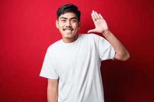 jovem lindo menino asiático vestindo camiseta branca renunciando dizendo olá feliz e sorridente, gesto de boas-vindas amigável foto