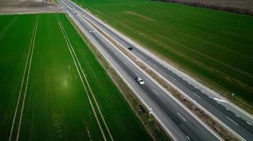 vista aérea do tráfego na estrada de duas pistas através do campo e campos cultivados foto