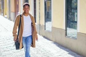 jovem negro andando na rua carregando uma maleta e um smartphone. foto