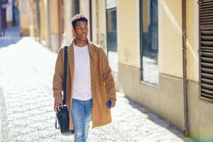 jovem negro andando na rua carregando uma maleta e um smartphone. foto