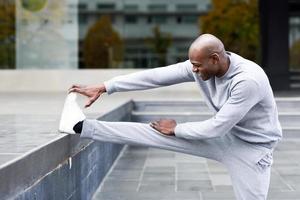 homem negro fazendo alongamento antes de correr em meio urbano foto