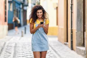 mulher norte-africana andando na rua olhando para seu telefone inteligente foto