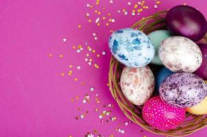 ovos de páscoa artesanais multicoloridos e confetes em fundo rosa. conceito mínimo. vista de cima. espaço para texto. foto de estúdio