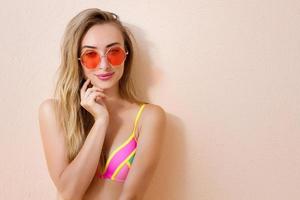 close-up de menina feliz em óculos de sol rosa isolados. férias de verão e fim de semana divertido. conceito de verão. jovem sorridente em maiô de moda. foco seletivo. roupa de verão de praia. espaço de cópia foto