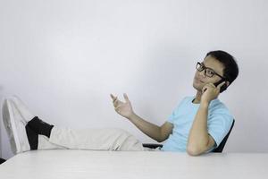 jovem asiático está se sentindo feliz e sorri quando fala ao telefone com a perna na mesa. foto