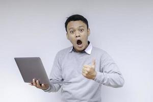 uau cara de jovem asiático chocou o que vê no laptop ao trabalhar isolado fundo cinza vestindo camisa cinza foto