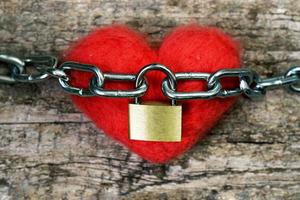 coração de brinquedo vermelho envolto com uma corrente e fechado com um cadeado de metal. conceito de amor. foto