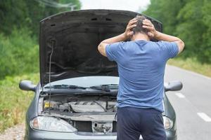 homem fica com as mãos na cabeça perto de seu carro quebrado foto