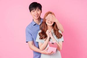jovem casal asiático segurando a caixa de presente rosa no fundo rosa foto