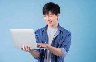 jovem asiático usando laptop em fundo azul foto