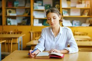 uma jovem sentada em uma mesa com uma camisa branca, um livro na mesa, uma bela estudante foto