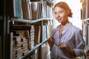 bela aluna fica entre as fileiras da biblioteca, foto