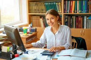 jovem senhora de negócios feliz na camisa branca, sentado à mesa com computador e papel ambiente de trabalho foto