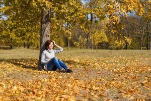 uma jovem de suéter cinza senta-se sozinha, encostada em uma árvore foto