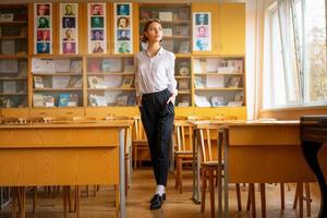 uma linda garota de camisa branca fica na sala de aula entre as mesas foto