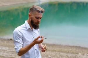 retrato de um cara barbudo bonito, acende um cigarro com um isqueiro ao ar livre foto