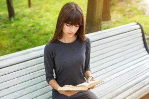 bela jovem sentada em um banco na rua lendo um livro foto