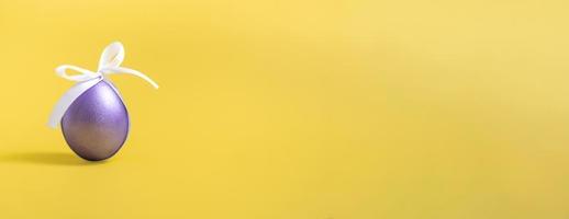 ovo de páscoa roxo com um laço branco em um fundo amarelo. espaço de cópia closeup. foto