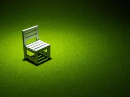 cadeira de madeira branca na grama artificial. luz brilhando de cima no tom escuro baixa chave foto