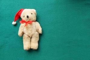 urso polar de brinquedo com chapéu de papai noel vermelho com um laço em um fundo verde. bandeira de natal. copie o espaço, lugar para texto, animal, panfleto, convite, flatlay foto