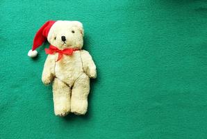 urso polar de brinquedo com chapéu de papai noel vermelho com um laço em um fundo verde. bandeira de natal. copie o espaço, lugar para texto, animal, panfleto, convite, flatlay foto