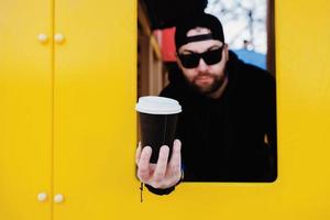 homem barbudo dá ao cliente caneca descartável foto